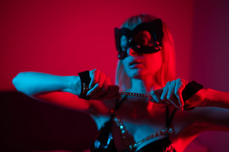 Frau in BDSM Katzenmaske und Handschellen vor rotem Hintergrund