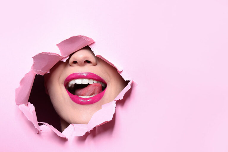Frau mit geschminkten Lippen schaut durch Loch in pinker Wand